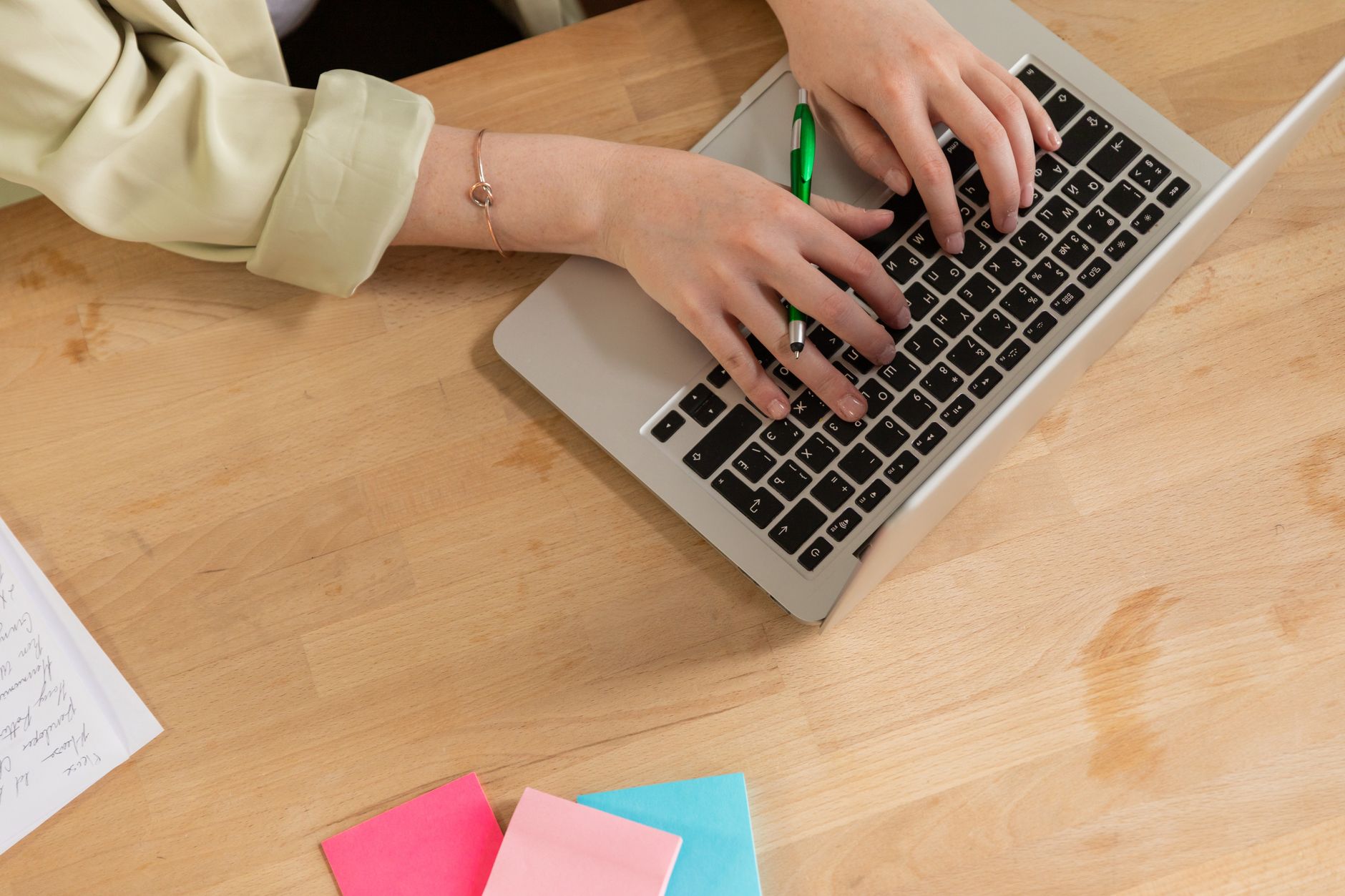Hands typing on a laptop with a green pen and colorful sticky notes on a wooden desk — illustrating: Best Green IT Consulting Firms for SMBs in Central Florida in 2026