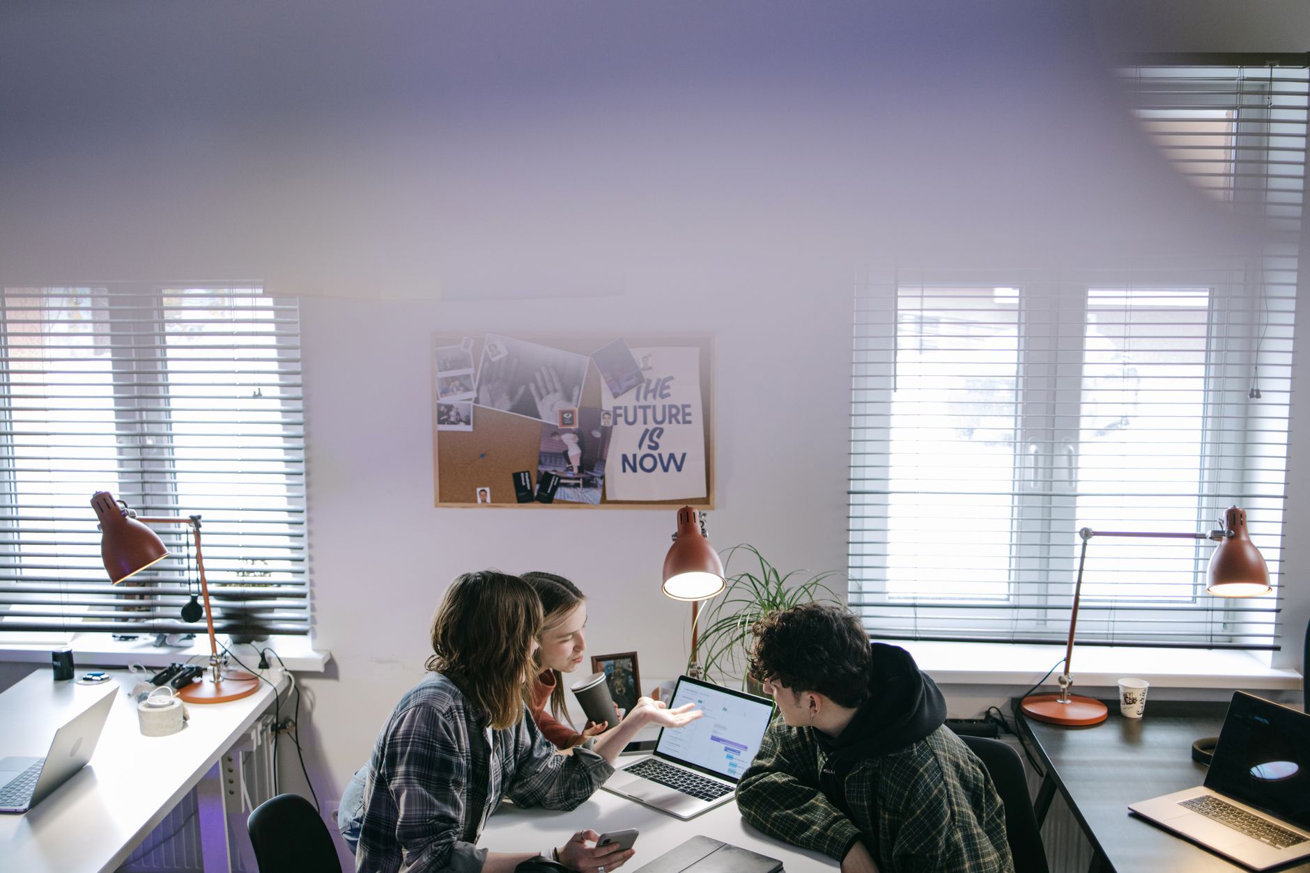 A group of people discussing ideas around laptops in a bright, modern office space — illustrating: Sustainable IT Solutions vs Traditional Managed Services: What Central Florida Businesses Really Need in 2025